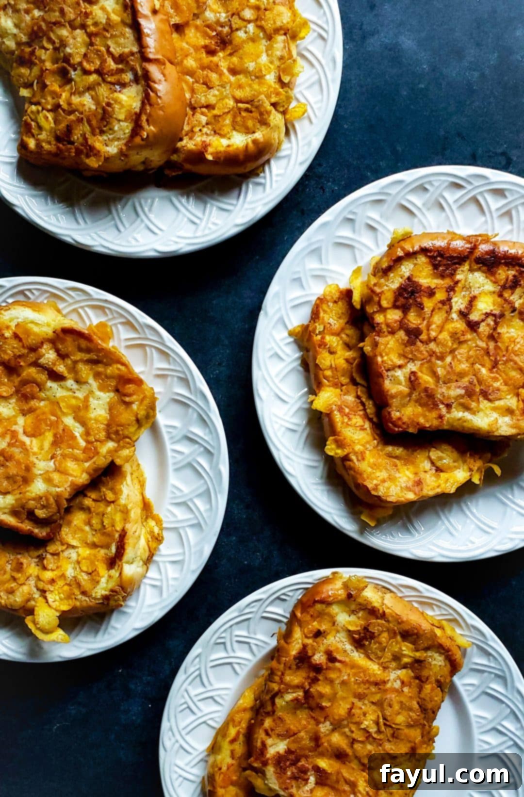 Four white plates on a blue counter with french toast on them. Each piece of french toast is golden brown and perfectly crispy, adorned with optional toppings like fresh fruit and whipped cream. The inviting setup promises a delightful breakfast or brunch experience for the whole family.