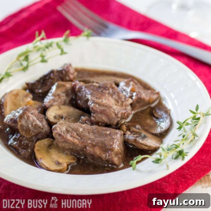 Side shot of crock pot beef and mushrooms in a white bowl garnished with herbs on a red cloth with a fork on the side.