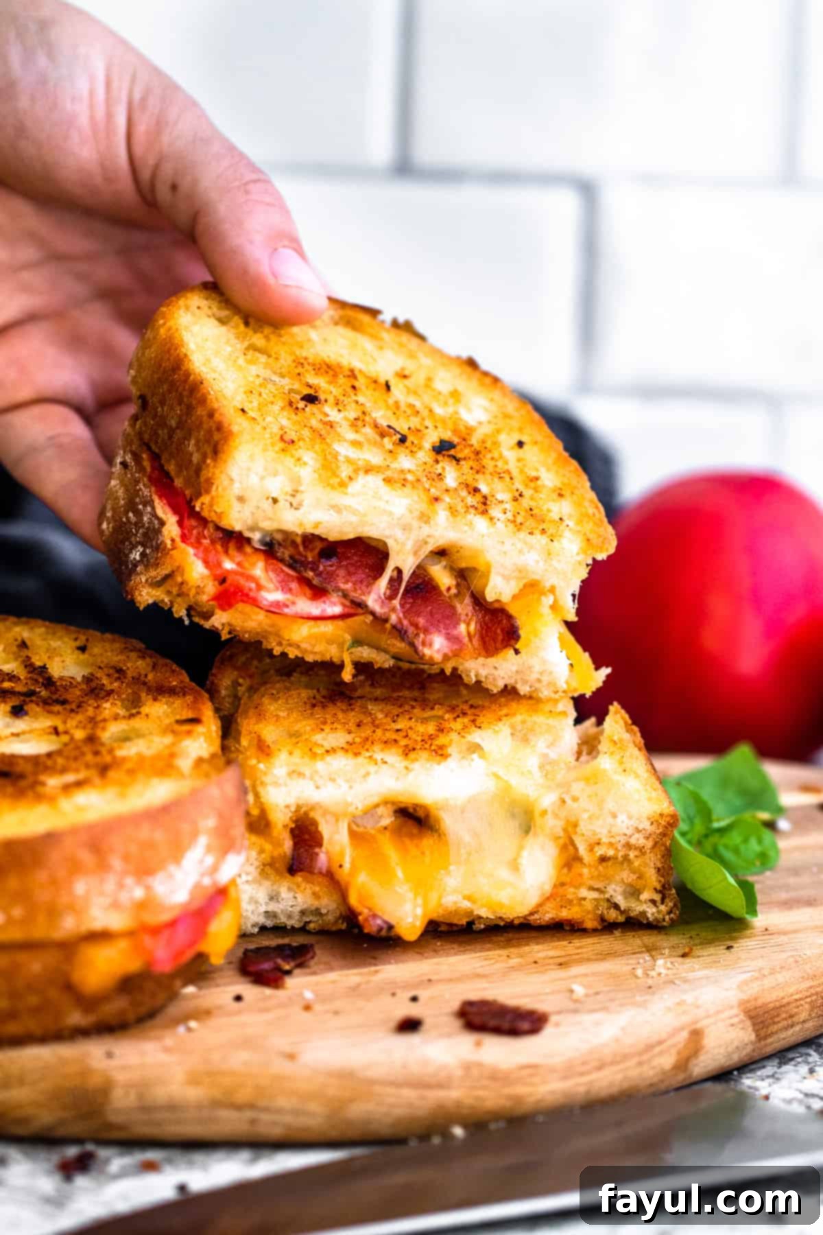 Hand picking up half of a crispy tomato bacon grilled cheese sandwich off a stack.