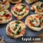 Angled close up shot of pepperoni pinwheels arranged on a metal baking sheet.