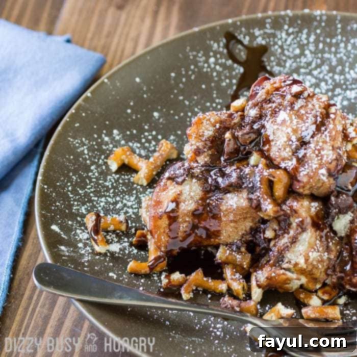 Close up shot of chocolate pretzel monkey bread on a grey plate sprinkled with powdered sugar with a fork on the side. 