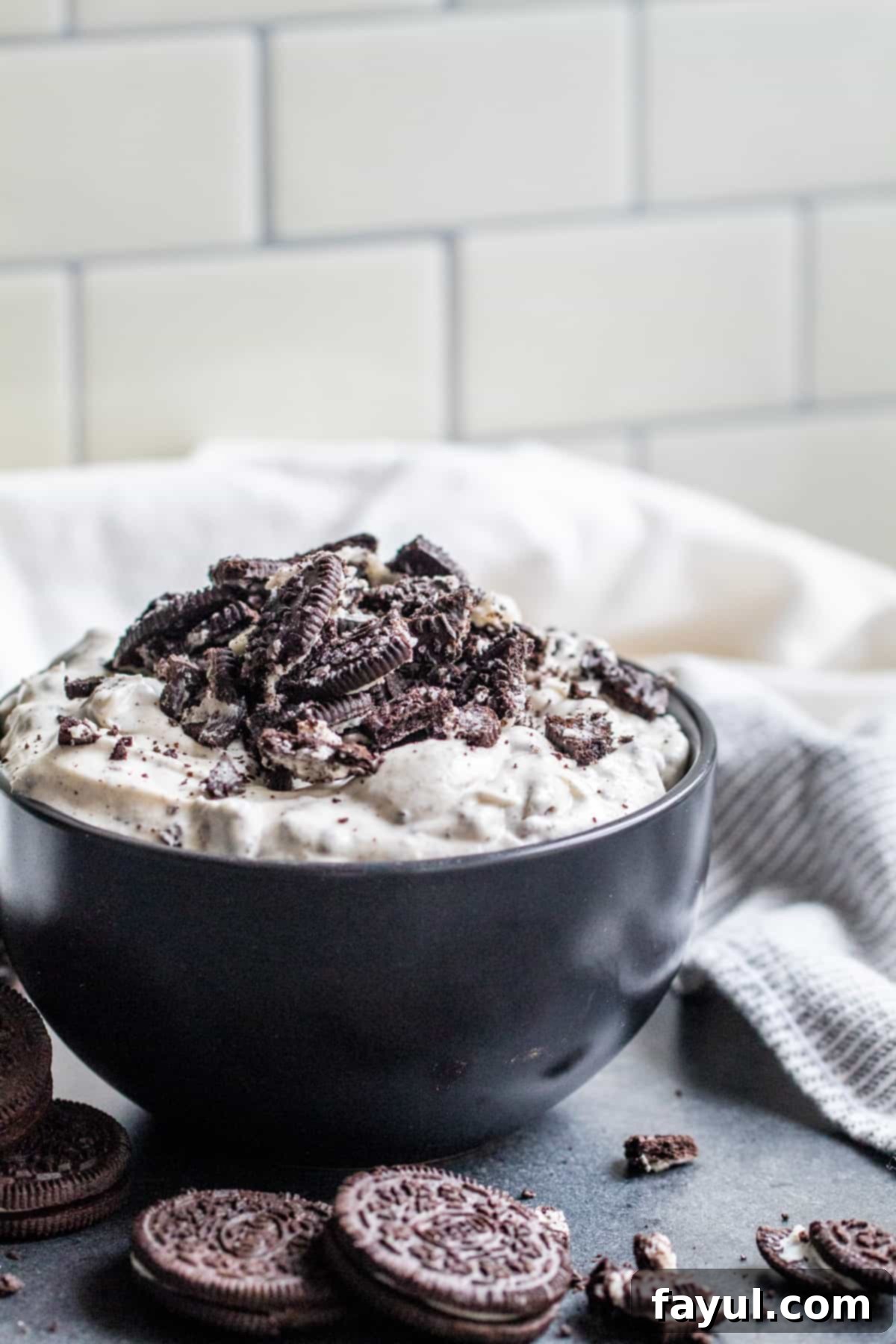 Effortless Oreo Dip Delight 2 Creamy Oreo dip in a black bowl, garnished with crushed Oreos and whole cookies, ready to serve on a dark gray table.