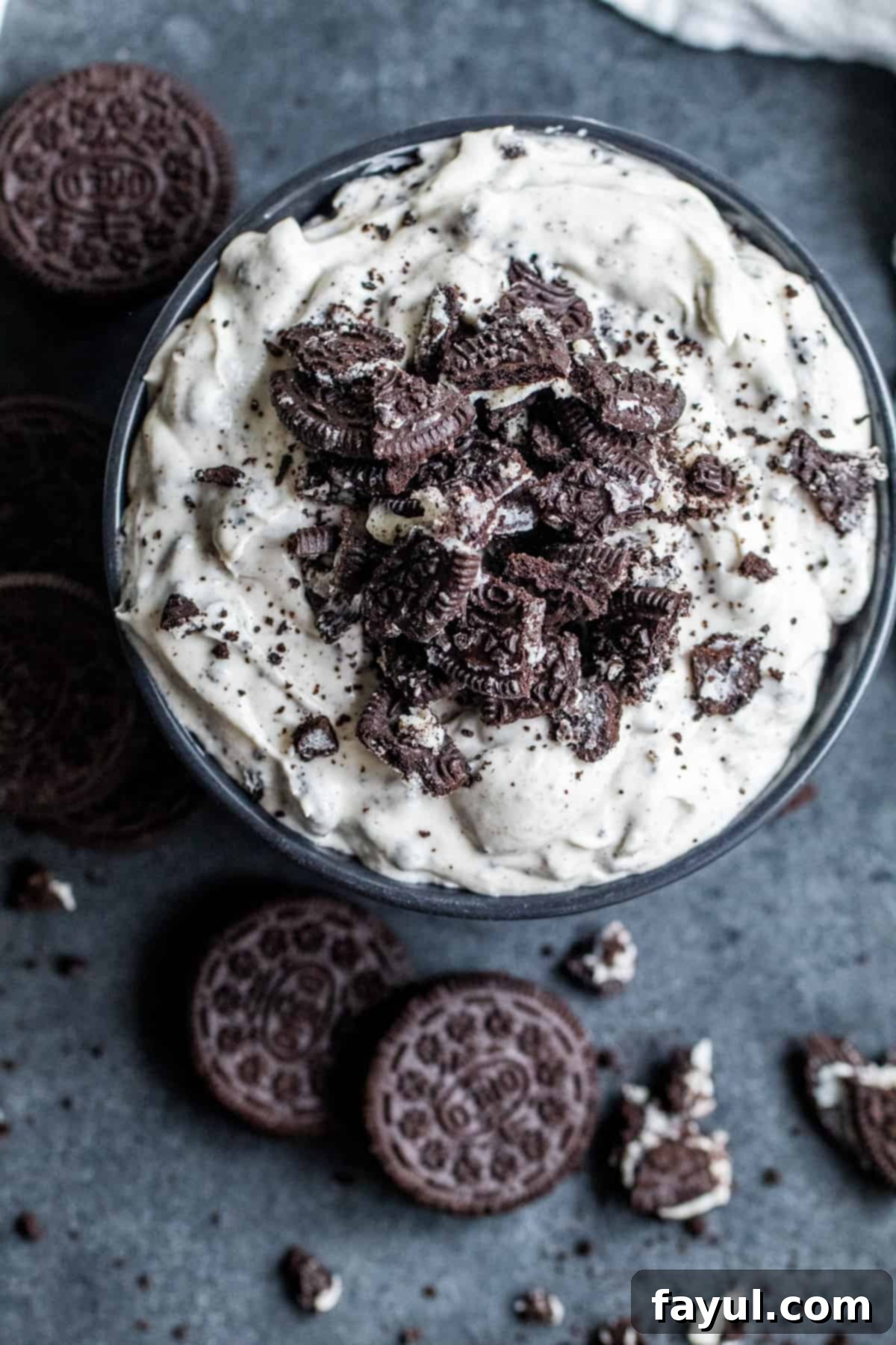 Effortless Oreo Dip Delight 5 Overhead shot of the finished Oreo dip in a black bowl on a counter, surrounded by whole and crushed Oreo cookies, ready for dipping.