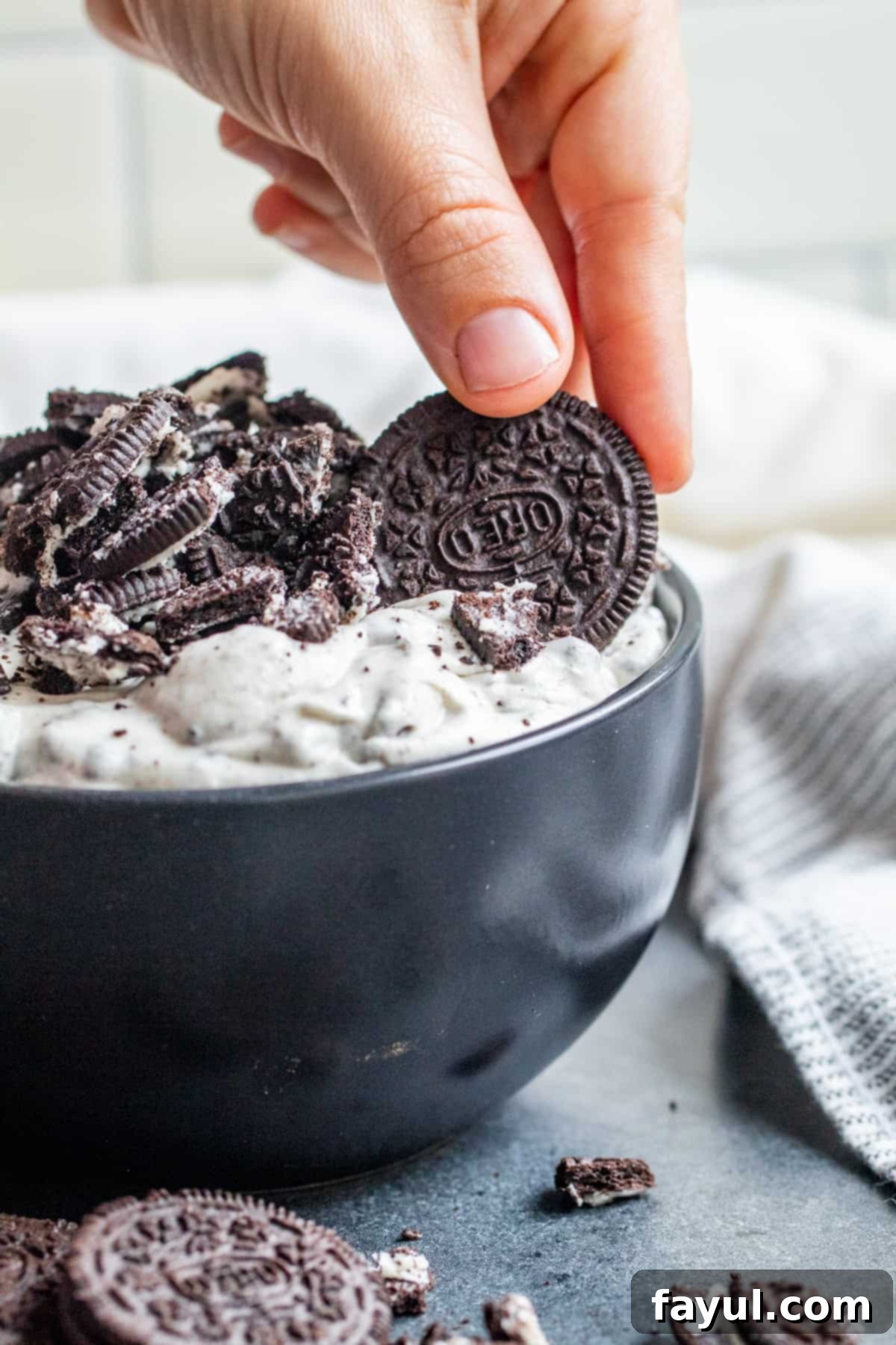 Effortless Oreo Dip Delight 6 A hand dipping a whole Oreo cookie into the creamy cookies and cream dip, highlighting its perfect consistency.