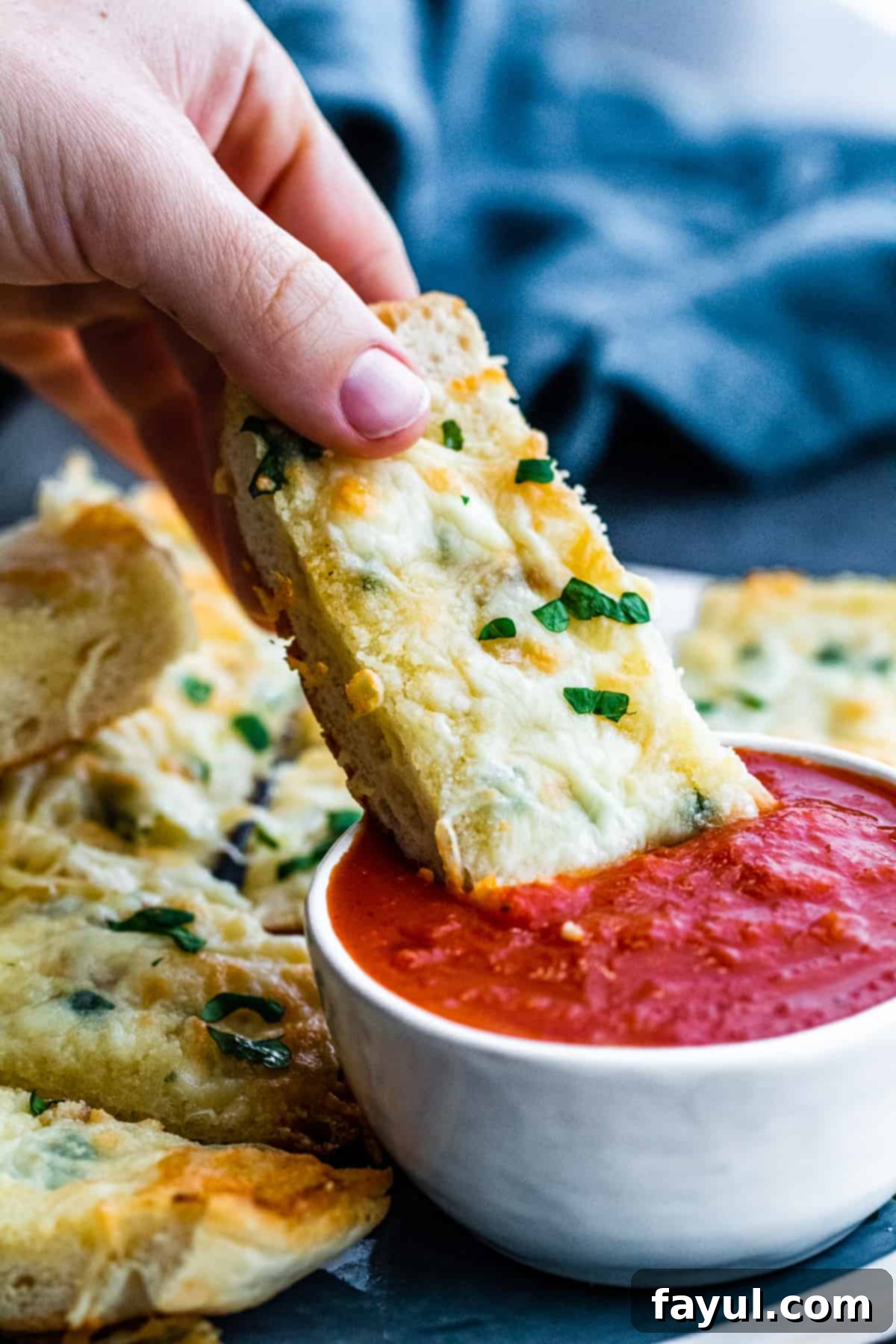 Hand dipping toasted cheese bread into bowl marinara sauce.