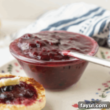 A jar of homemade Triple Berry Jam on a light surface with fresh berries