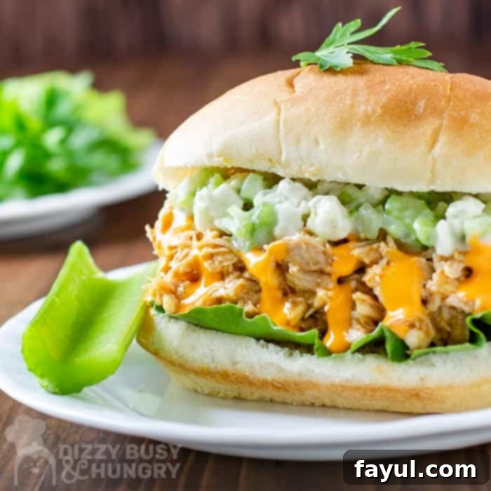 Side view of buffalo chicken sandwich with a side of celery on a white plate and wooden background.