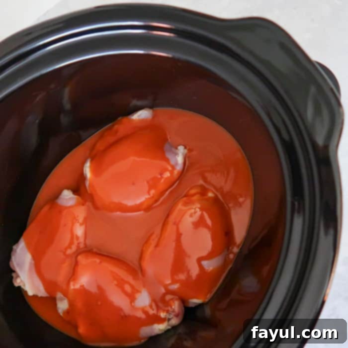 Close up shot of chicken covered with buffalo chicken sauce in a black crock pot.