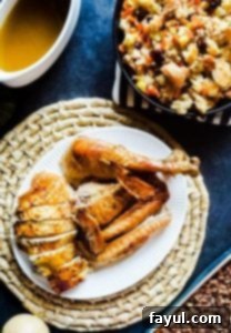 A beautifully golden herb butter roasted turkey sits on a white serving platter, surrounded by various festive side dishes on a blue counter. The turkey is perfectly cooked and ready to be carved.