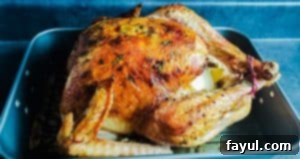 A perfectly golden-brown herb butter roasted turkey sits in a silver roasting pan on a wire rack, ready for the holiday feast. The shot is taken at a 45-degree angle on a blue countertop.