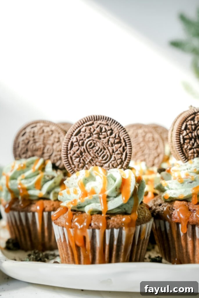 A perfectly piped Grasshopper Caramel Cupcake with green mint Oreo buttercream, a whole Oreo cookie, and a glistening drizzle of salted caramel on a white plate.