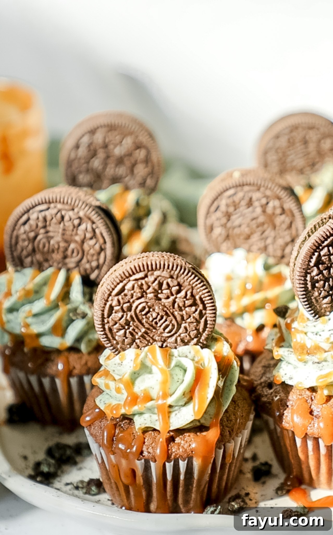A professional baker piping green mint Oreo buttercream onto a chocolate cupcake using a piping bag and a star tip, creating a perfect swirl.