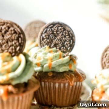 A beautifully decorated Grasshopper Caramel Cupcake with a tall swirl of green mint Oreo buttercream, topped with an Oreo and caramel drizzle, ready to be served.