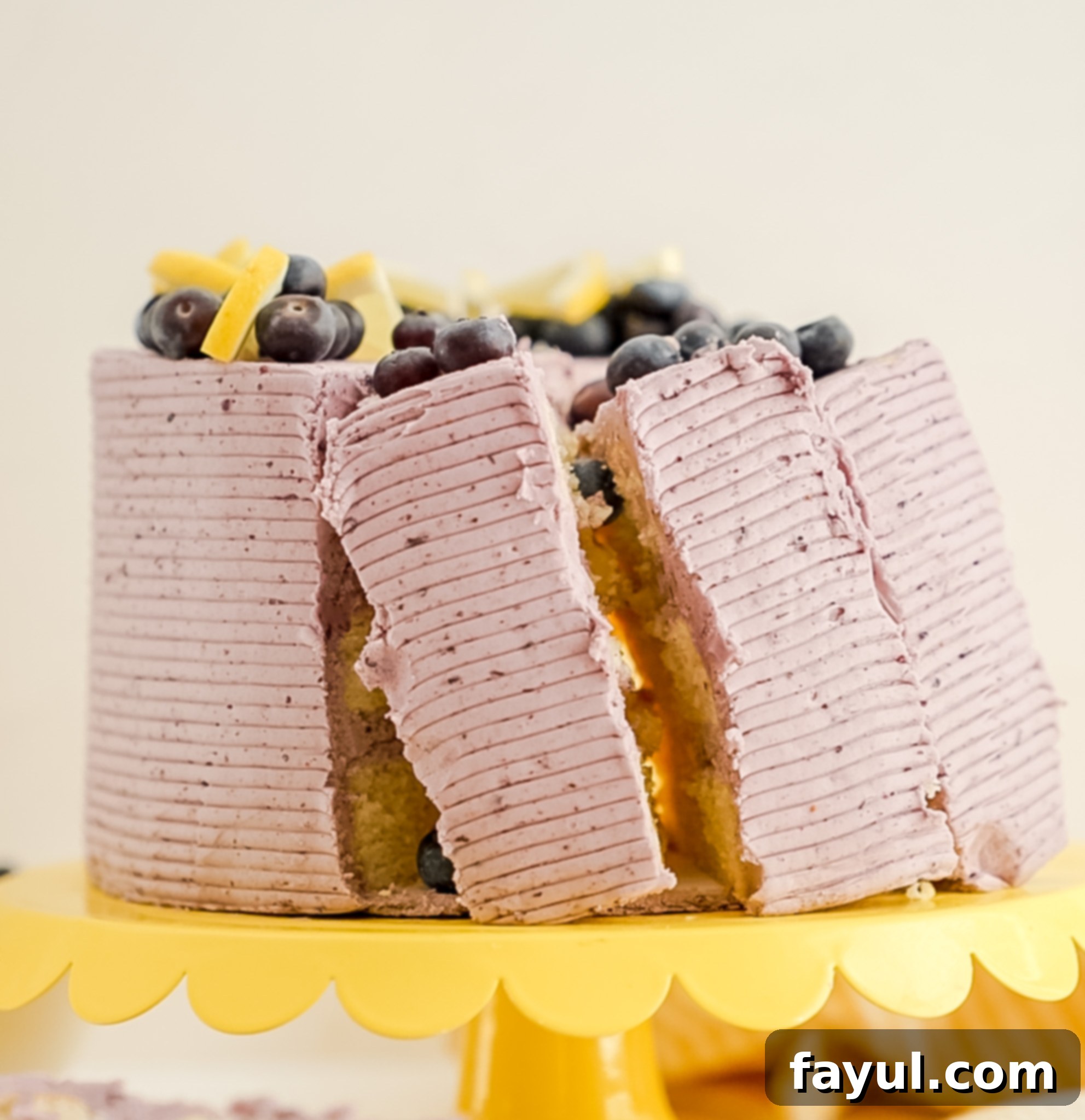 Close-up of a slice of Lemon Blueberry Cake, showing the fluffy lemon layers, thick lemon curd, and purple blueberry frosting.