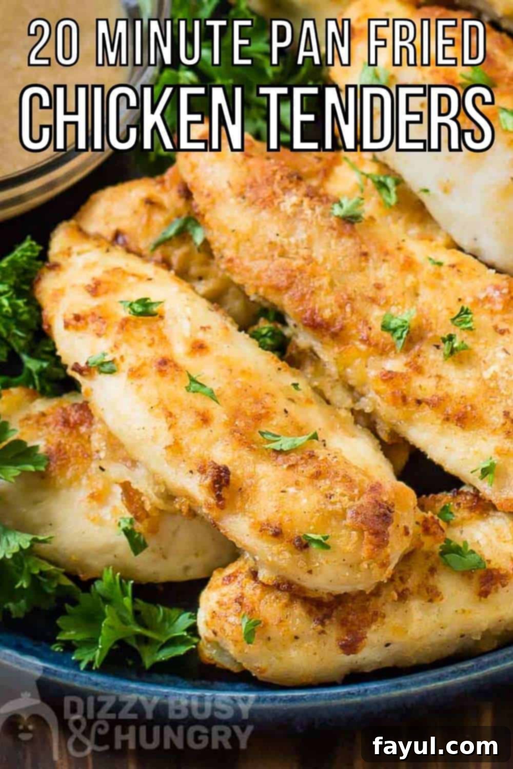 Close up shot of golden brown pan-fried chicken tenders on a bed of fresh greens on a black plate, with a small clear bowl of rich, brown gravy on the side, all arranged on a rustic wooden surface.