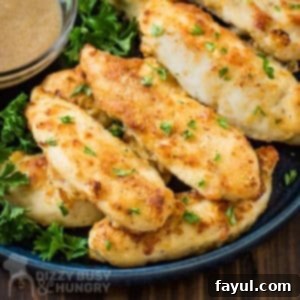 Close up shot of chicken tenders on a bed of greens on a black plate with a clear bowl of gravy on the side on a wooden surface.