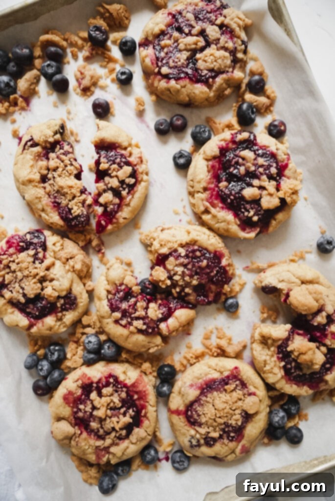 A single browned butter blueberry cookie broken in half, showing the gooey blueberry filling
