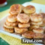 Pan fried banana snacks piled on a white square dish and placed on yellow and green napkins.