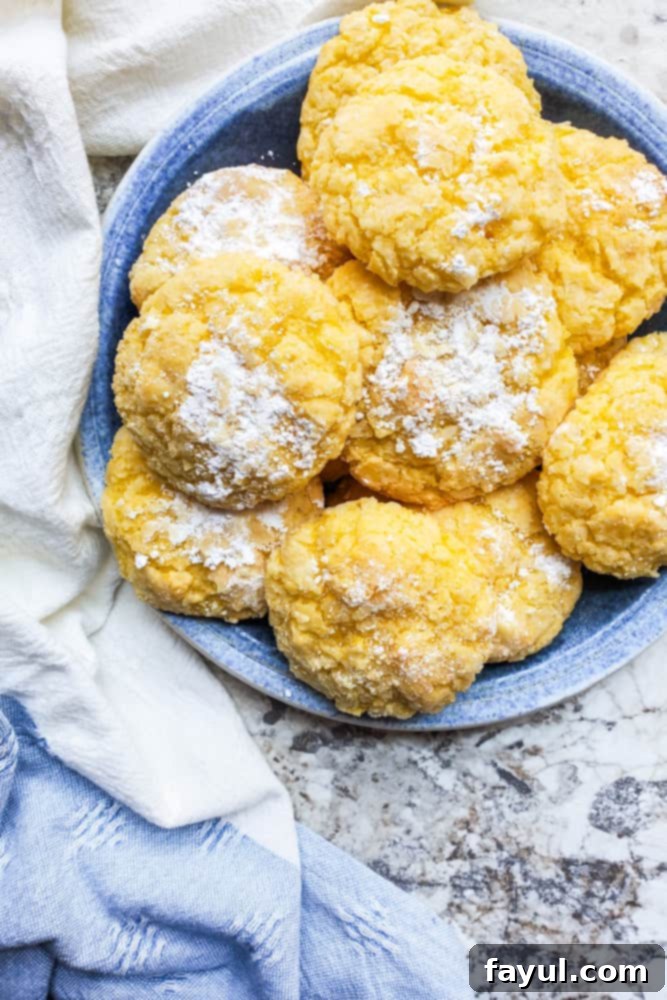 A blue plate elegantly showcasing a stack of freshly baked Gooey Butter Cake Cookies, lightly dusted with powdered sugar, set against a pristine white kitchen counter. The cookies have a signature crackled top and a soft, inviting texture.