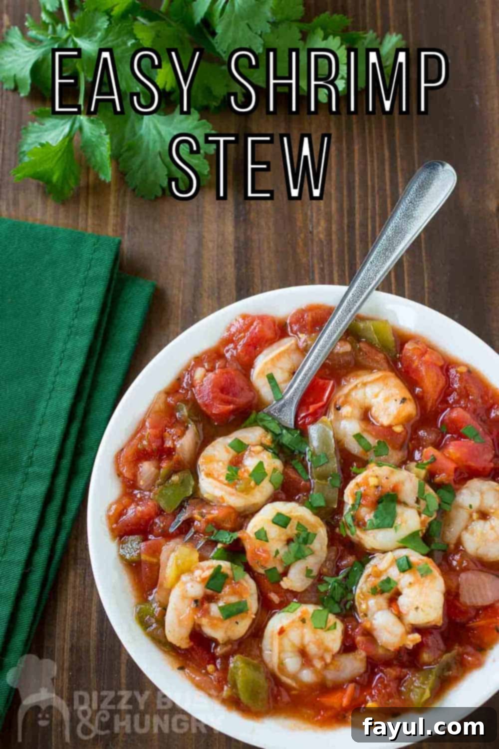 Overhead close up shot of shrimp stew garnished with herbs in a white bowl with a spoon on the side and green napkin and herbs by the bowl on a wooden surface. A vibrant and appetizing shrimp stew.