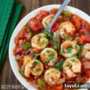 Overhead shot of shrimp stew sprinkled with herbs in a white bowl with a green cloth on the side.