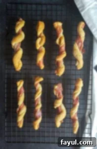 Prep image for Prosciutto Wrapped Breadsticks with Gouda Cheese Dip. The image shows the finished bread twists cooling on a black backing wire rack. The rack is sitting on a dark brown counter top and there is a white cloth on the right side.