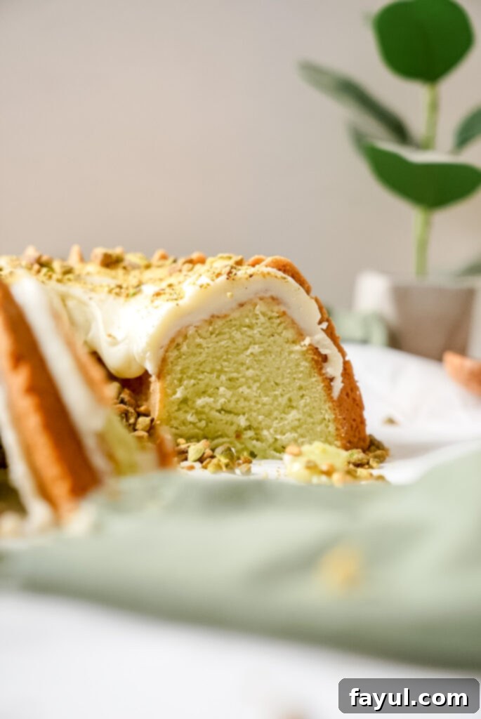 A close-up of a slice of moist lemon pistachio bundt cake, showing its vibrant green interior and a generous drizzle of lemon cream cheese glaze.