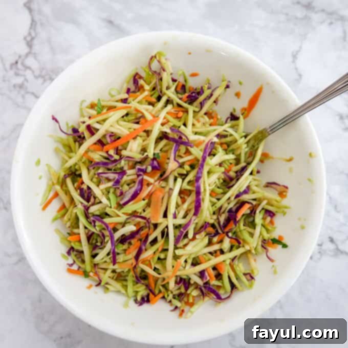 Overhead view of colorful broccoli slaw with carrot and red cabbage shreds, tossed in a light dressing, in a medium white bowl.