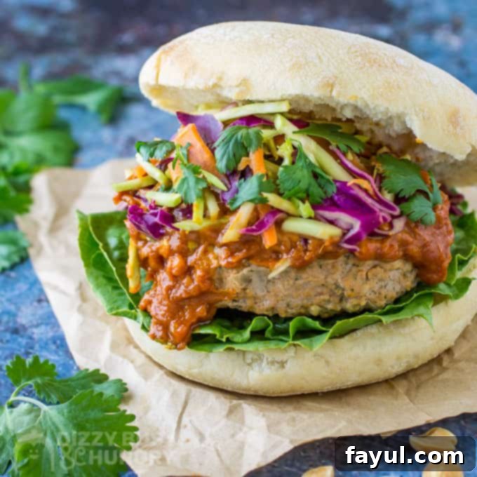 Side angle view of a beautifully assembled Thai turkey burger on a bun, generously topped with creamy peanut sauce and crunchy Asian-style slaw.