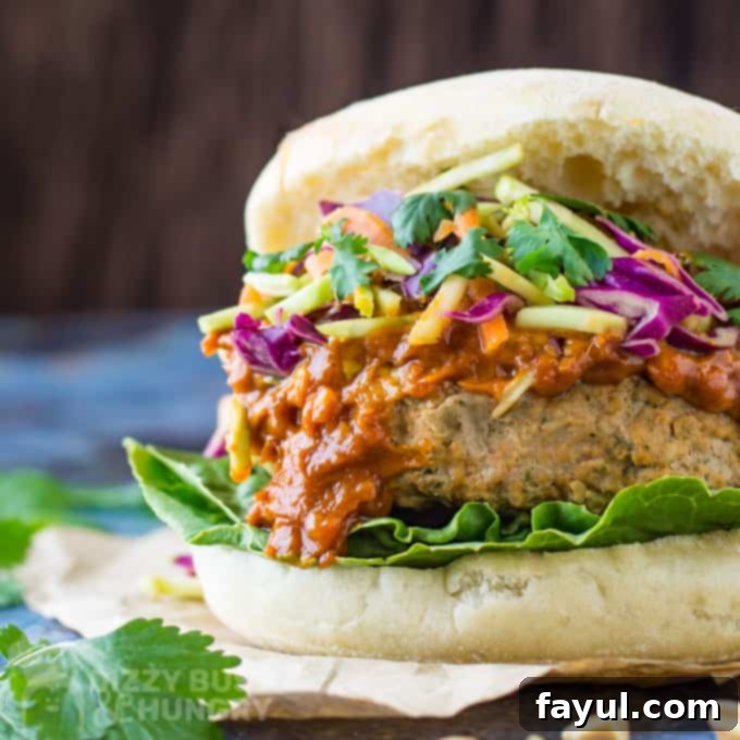 Front angle view of a Thai turkey burger, piled high with rich peanut sauce and vibrant Asian-style slaw, nestled on a bed of fresh lettuce.