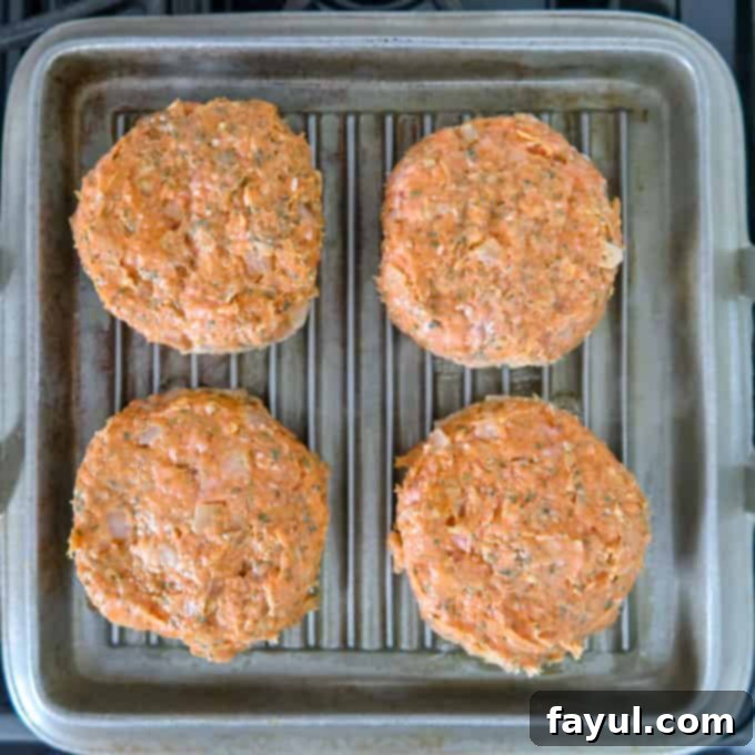 Overhead view of 4 perfectly formed Thai turkey burger patties, sizzling on the grill top, ready to be cooked to perfection.