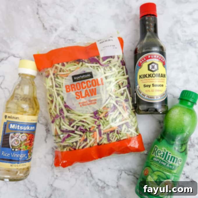Overhead view of rice vinegar, broccoli slaw, soy sauce, and lime juice, laid out for the Asian-style slaw.