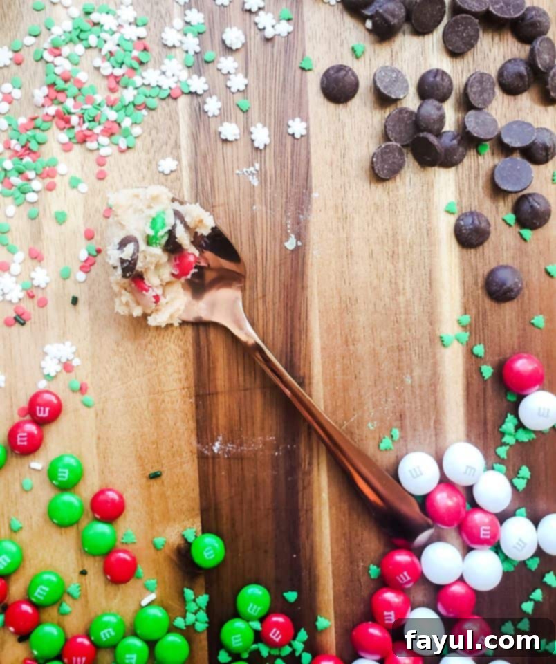 Overhead shot of edible cookie dough on a gold spoon with candy, sprinkles and chocolate surrounding it, highlighting delicious add-ins.