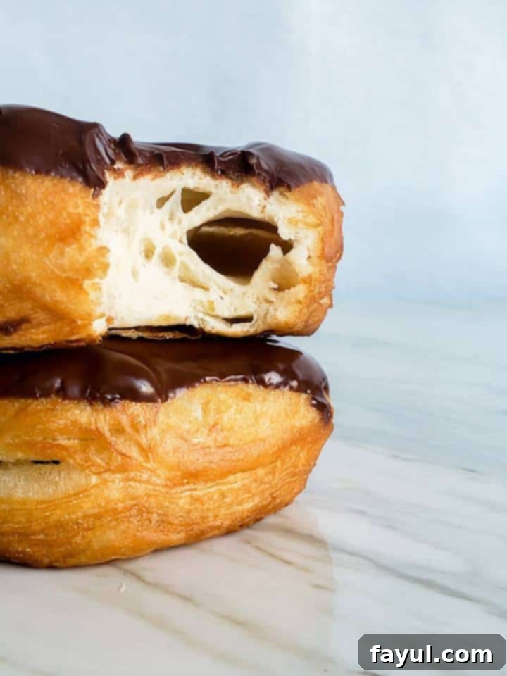 A stack of three homemade chocolate glazed donuts, with a bite taken out of the top one, revealing the soft interior.