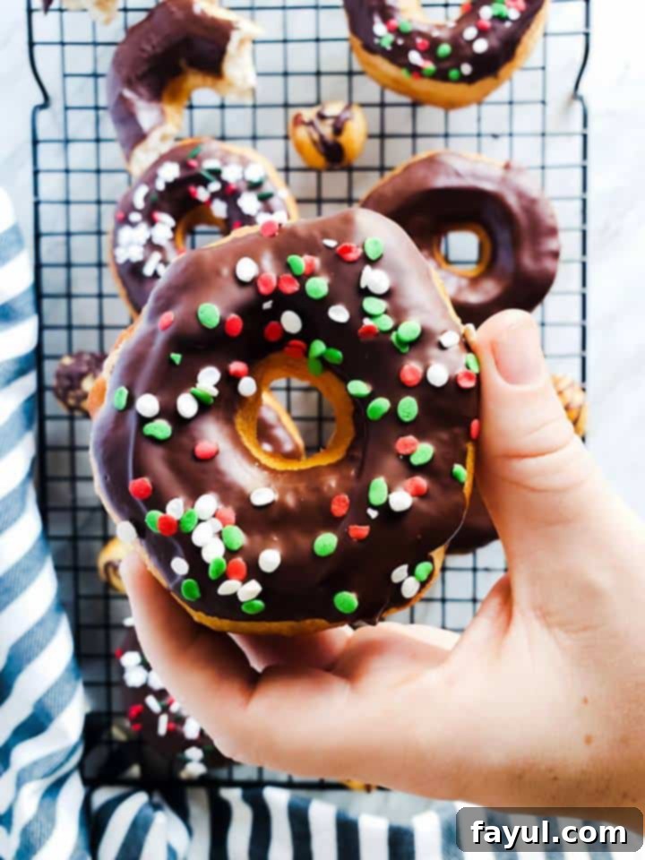 A hand presenting a freshly made chocolate glazed biscuit donut with sprinkles.