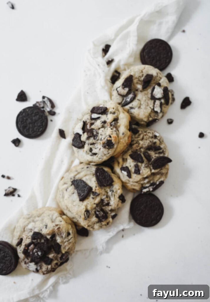 A freshly baked bakery style Oreo chocolate chip cookie being gently broken in half, revealing its soft, warm interior with melted chocolate and crunchy Oreo pieces.