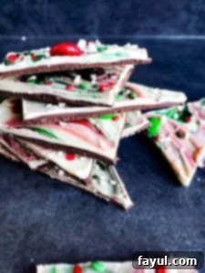 Image for Christmas chocolate bark recipe, taken at an angle, showing pieces stacked on a blue counter with vibrant toppings.
