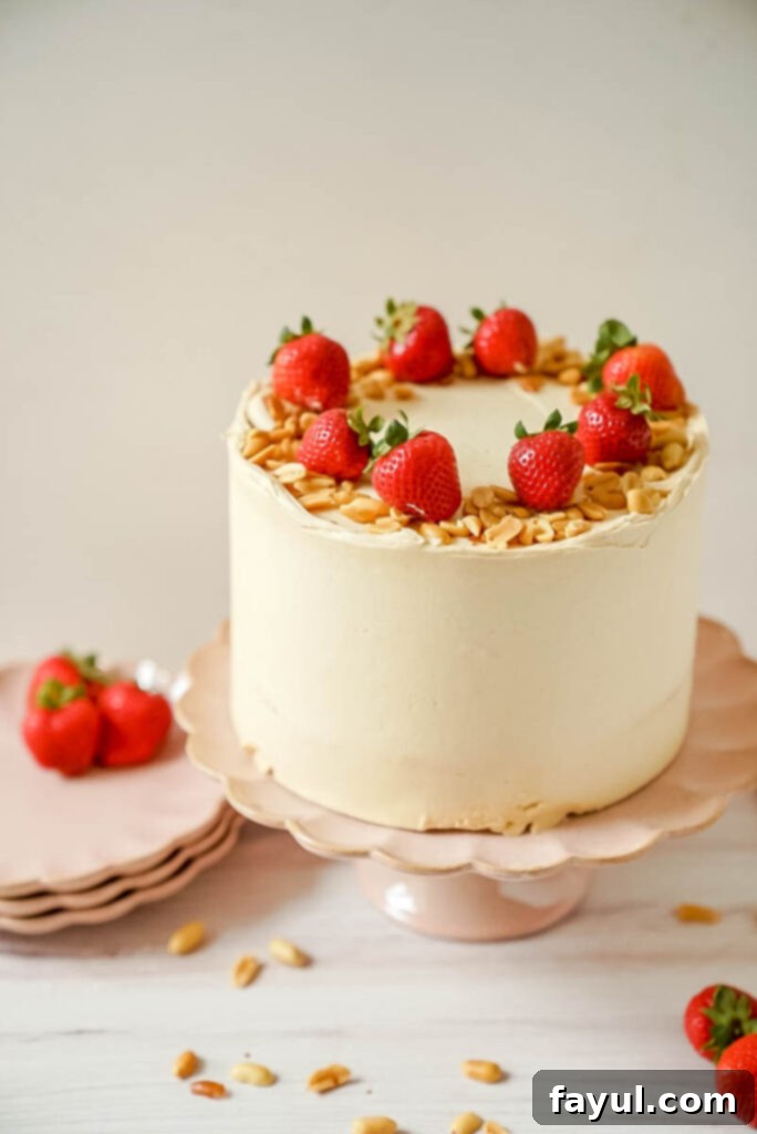 Beautifully decorated three-layer Peanut Butter and Jelly Cake, showcasing the rich peanut butter frosting and a hint of strawberry jam peeking out.