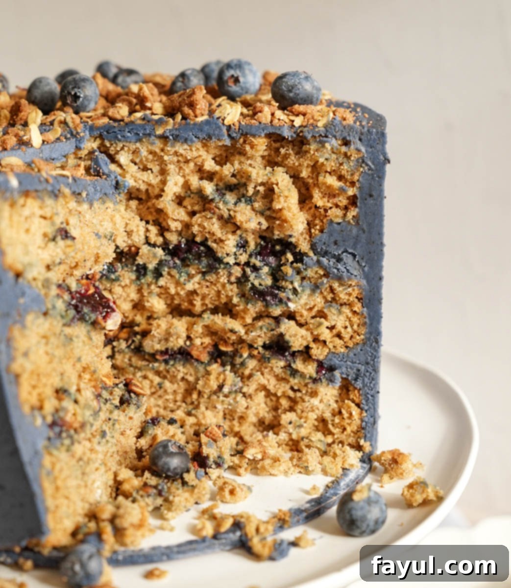 A perfectly cut slice of Blueberry Crisp Cake, revealing the distinct layers of cake, blueberry compote, and oat crumble.