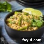 Side shot of cilantro lime brown rice with asparagus, garnished with fresh cilantro and lime wedges, served in a stylish black bowl.