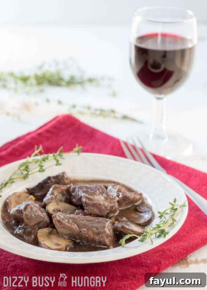 Side view of savory Crock Pot beef and mushrooms, elegantly plated on a white dish with herbs sprinkled around and a fork on the side.