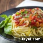 Side shot of pasta adorned with a rich red mushroom sauce, garnished with fresh basil on a sleek black plate.