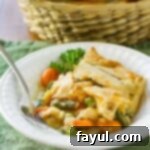 Side view of a comforting portion of chicken pot pie served in a white bowl with a fork, against a soft green background.