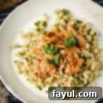 Overhead view of creamy butter chicken served over fluffy couscous, garnished with fresh herbs in a pristine white bowl.