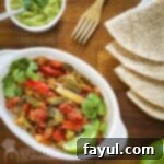 Overhead shot of vibrant veggie fajitas served in a white dish, garnished with fresh cilantro, alongside warm tortillas and creamy guacamole.