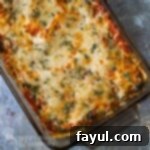 Overhead shot of a baked ravioli casserole, garnished with fresh herbs, served in a baking dish on a blue marble surface.