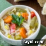 Close-up shot of comforting chicken soup served in a white bowl, resting on a green napkin.