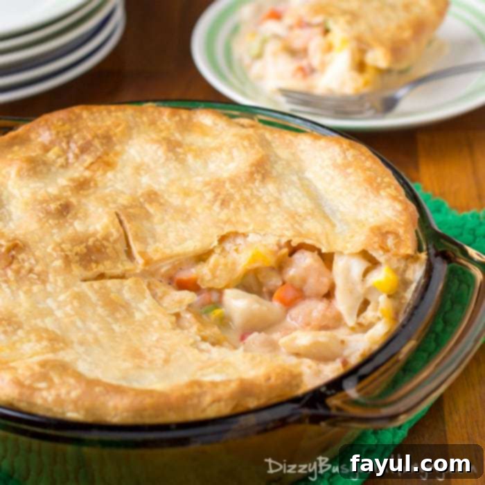Side view of a golden-crusted whole seafood pot pie, with a slice removed to reveal the rich filling, blurred in the background.