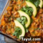 Overhead shot of a finished Dorito casserole in a pan, beautifully garnished with fresh chopped cilantro and avocado slices.