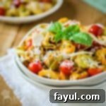 Side angled shot of tortellini garnished with fresh basil and Parmesan cheese, served in a white bowl nested within another, on a white cloth atop a wooden table.